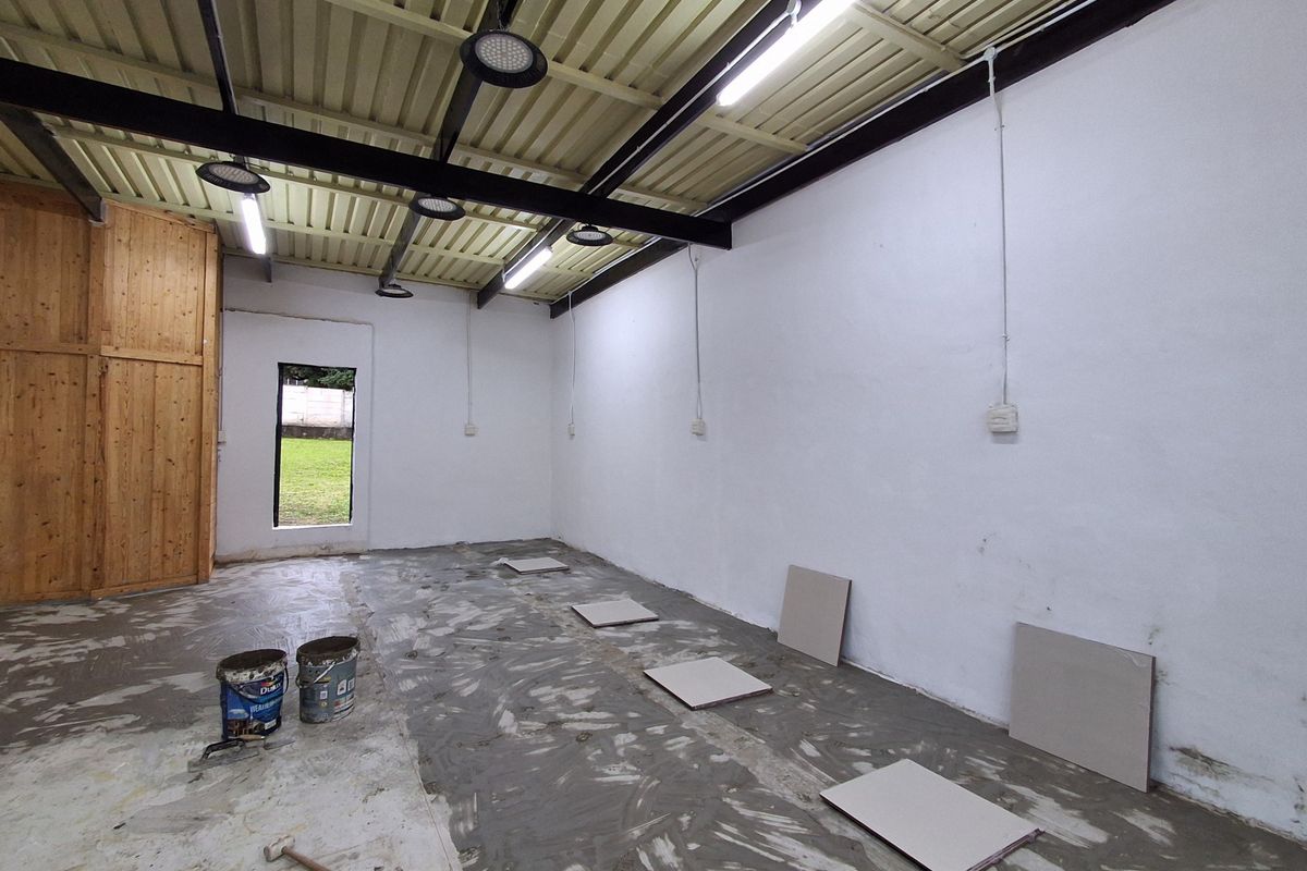 An unfinished utility space featuring exposed steel beams, corrugated metal ceiling, and basic electrical infrastructure, currently undergoing floor renovation.