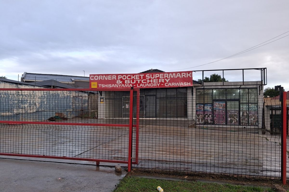 Front view of a commercial retail property featuring a paved forecourt, secure metal fencing, and prominent signage for a supermarket and butchery.