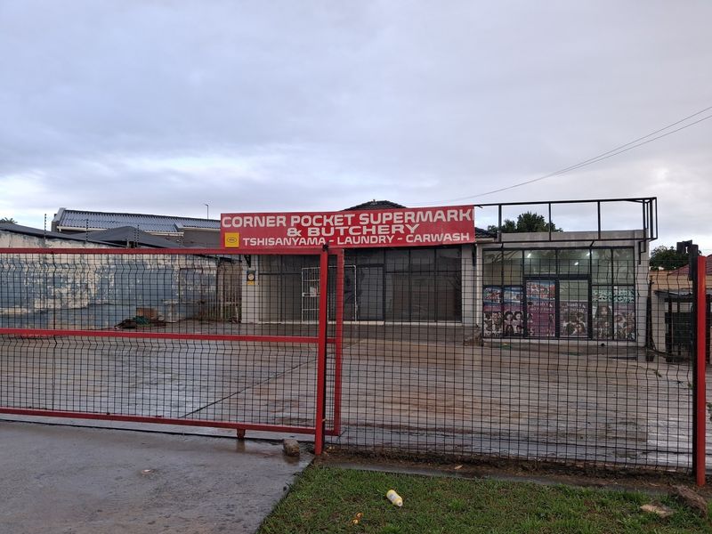 Front view of a commercial retail property featuring a paved forecourt, secure metal fencing, and prominent signage for a supermarket and butchery.
