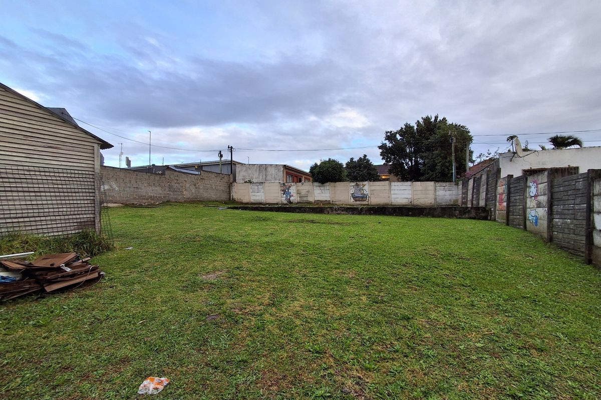 A spacious rear yard area enclosed by precast concrete boundary walls, featuring a grass lawn and visible graffiti on the perimeter fencing.