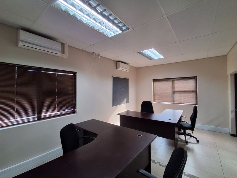 A functional office space featuring tiled flooring, suspended ceilings with recessed lighting, and dual split-system air conditioning units for climate control.