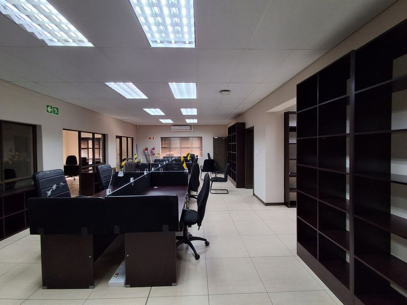 A spacious, well-lit open-plan office area featuring tiled flooring, built-in shelving, and integrated ceiling lighting, suitable for a professional workspace.
