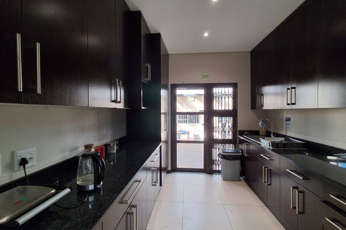 A modern office kitchen featuring dark wood cabinetry, granite countertops, stainless steel sink, and direct access to an outdoor area via a security gate.