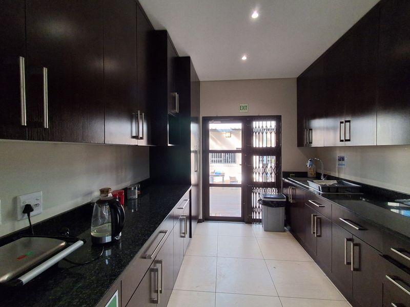 A modern office kitchen featuring dark wood cabinetry, granite countertops, stainless steel sink, and direct access to an outdoor area via a security gate.