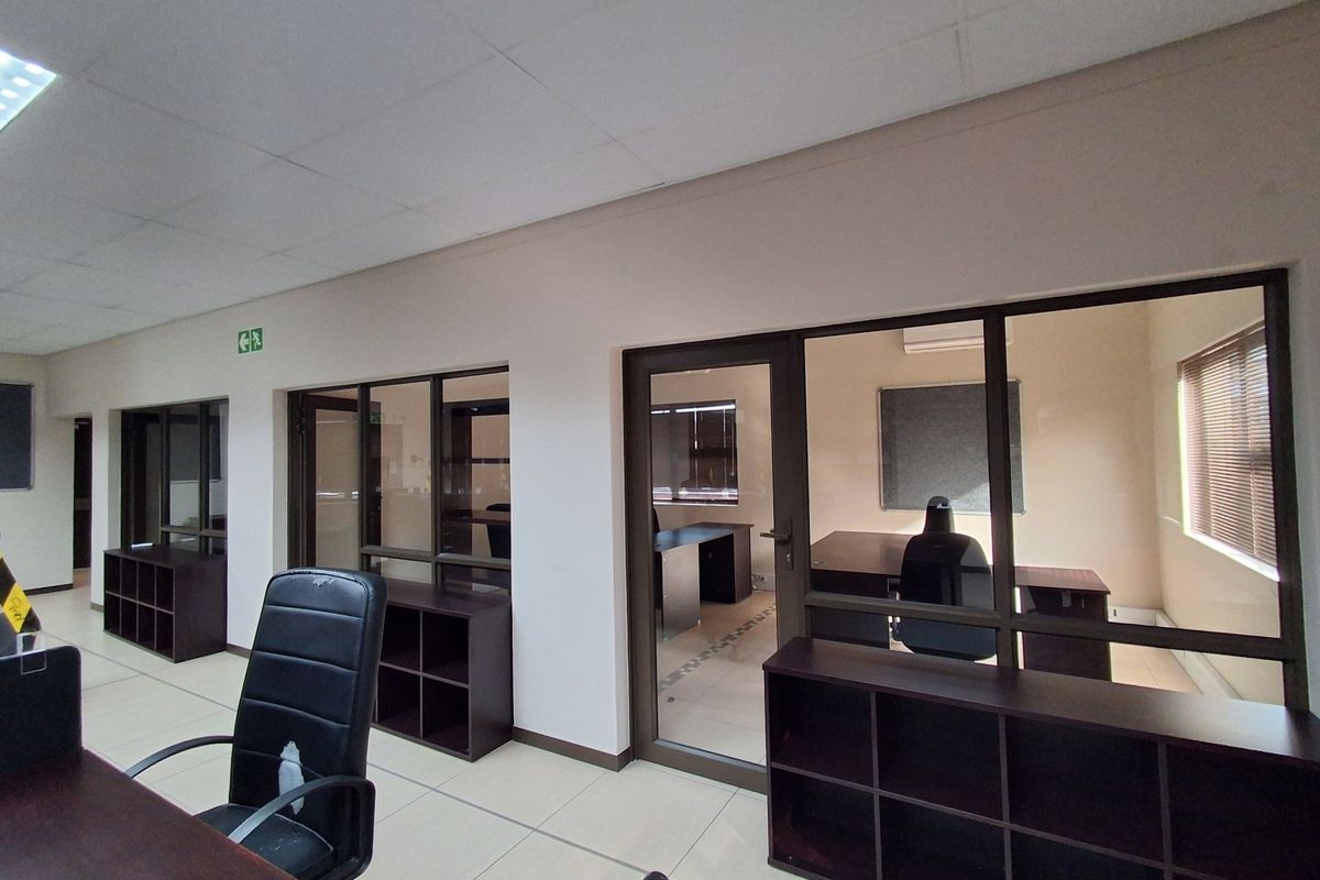 Professional office space featuring glass partitions, built-in storage shelving, tiled flooring, and a suspended ceiling with integrated lighting.