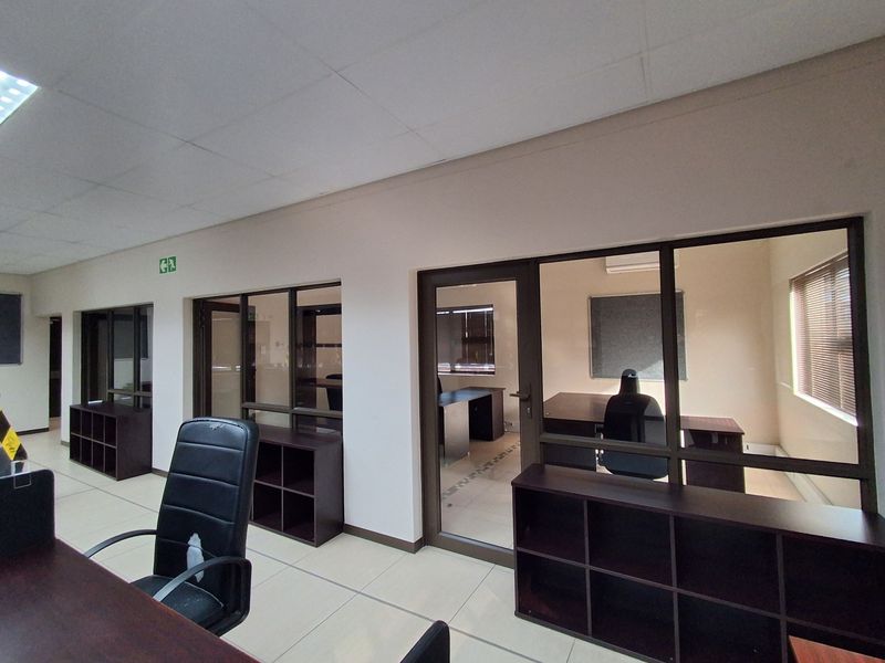 Professional office space featuring glass partitions, built-in storage shelving, tiled flooring, and a suspended ceiling with integrated lighting.