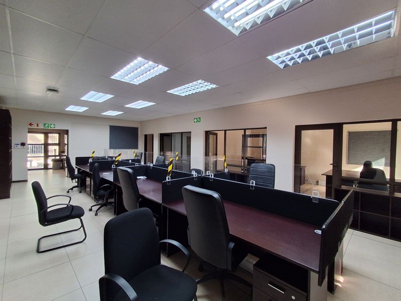 A professional open-plan office space featuring tiled flooring, suspended ceilings with recessed lighting, and integrated glass-partitioned workstations.