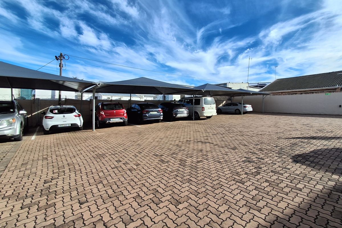 A paved parking area featuring multiple shade cloth carports, enclosed by a perimeter wall with security fencing.