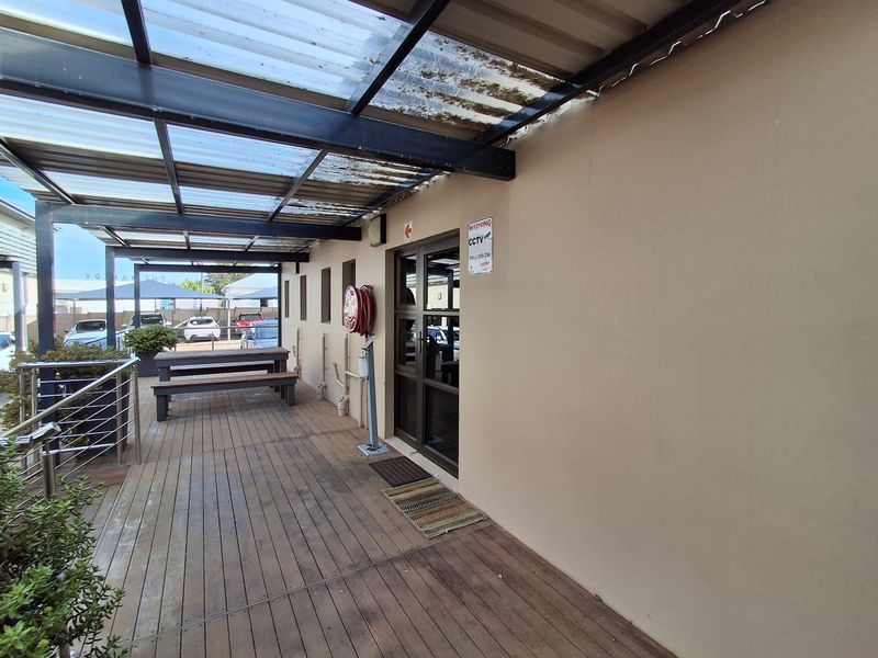 Covered outdoor patio area featuring timber decking, a corrugated roof structure, and a fire hose reel, providing a functional exterior entrance space.