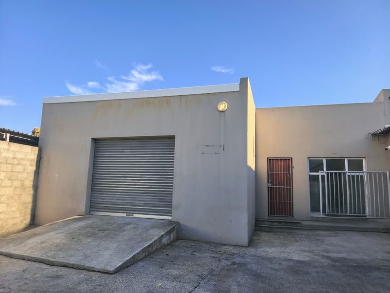 Industrial property exterior featuring a roller shutter door, concrete access ramp, and secure entrance door with security gate.