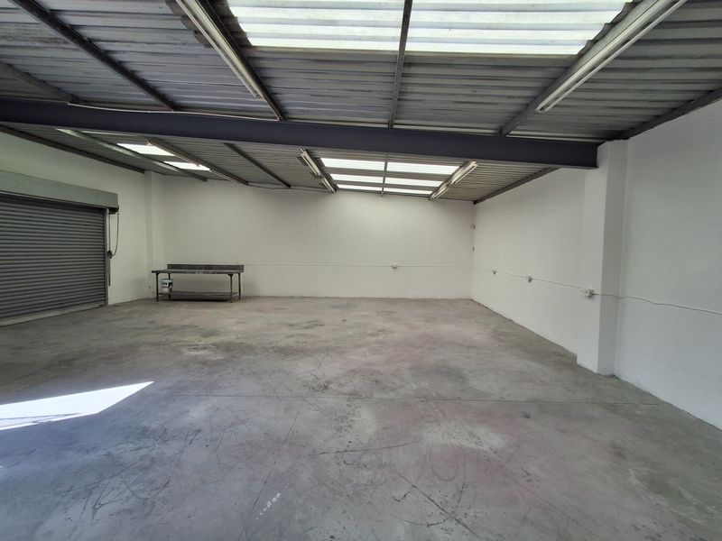 A spacious, empty industrial utility area featuring concrete flooring, exposed steel roof structure with translucent panels, and a large roller shutter door.