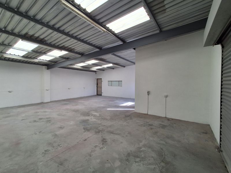Spacious industrial utility area featuring high ceilings with skylights, exposed steel beams, and durable concrete flooring, suitable for storage or workshop use.