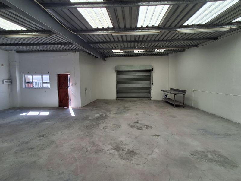 Spacious industrial utility area featuring concrete flooring, exposed steel roof structure with translucent panels, and a secure roller shutter door.