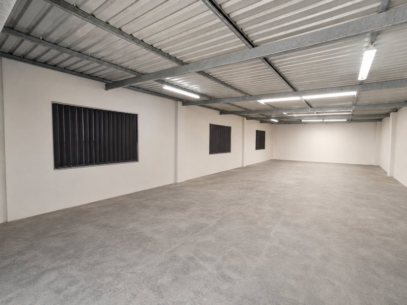 A clean, open-plan industrial utility space featuring exposed steel roof beams, polished concrete flooring, and functional strip lighting.
