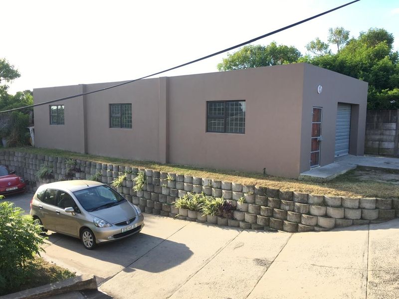 Exterior view of an industrial building featuring a concrete retaining wall, security gates, and a roller shutter door access point.