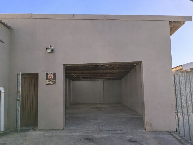 Industrial garage space featuring concrete flooring, exposed timber ceiling beams, and a side access door, suitable for storage or workshop use.