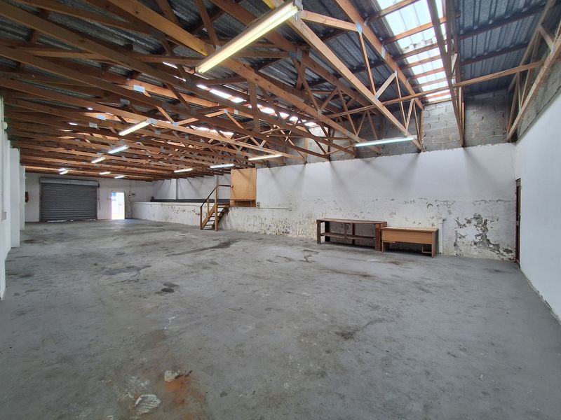 Spacious industrial utility area featuring exposed timber roof trusses, concrete flooring, and a roller shutter door, suitable for storage or workshop use.