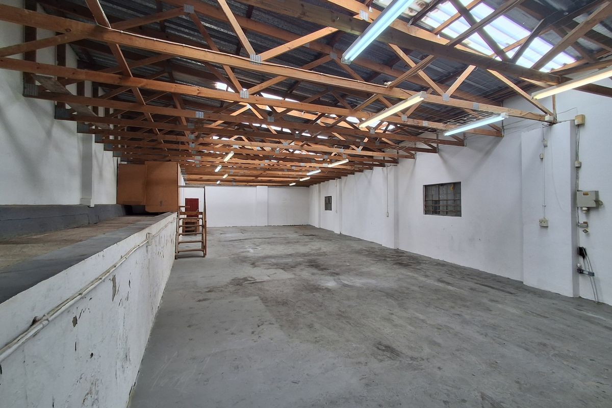 Spacious industrial utility area featuring exposed timber roof trusses, concrete flooring, and functional strip lighting, suitable for storage or workshop use.