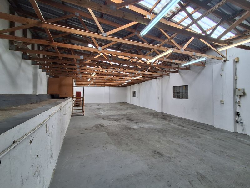 Spacious industrial utility area featuring exposed timber roof trusses, concrete flooring, and functional strip lighting, suitable for storage or workshop use.