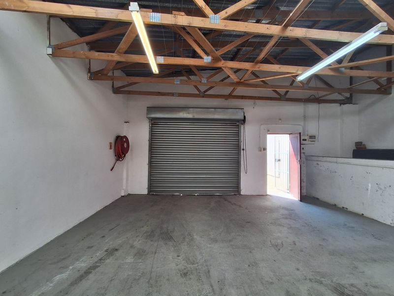 Spacious industrial garage featuring exposed timber roof trusses, concrete flooring, a roller shutter door, and a wall-mounted fire hose reel.