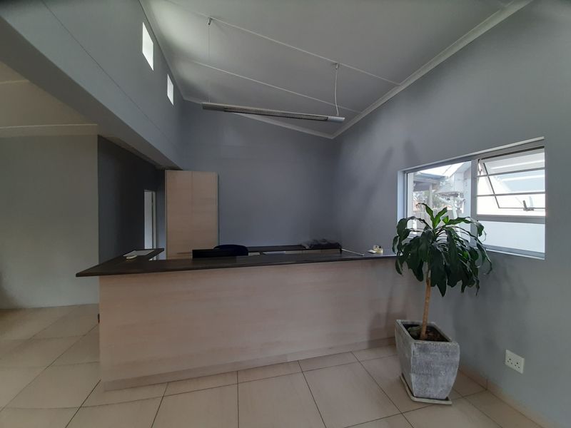 A clean, professional office space featuring a built-in reception desk, tiled flooring, and ample natural light from clerestory and louvered windows.