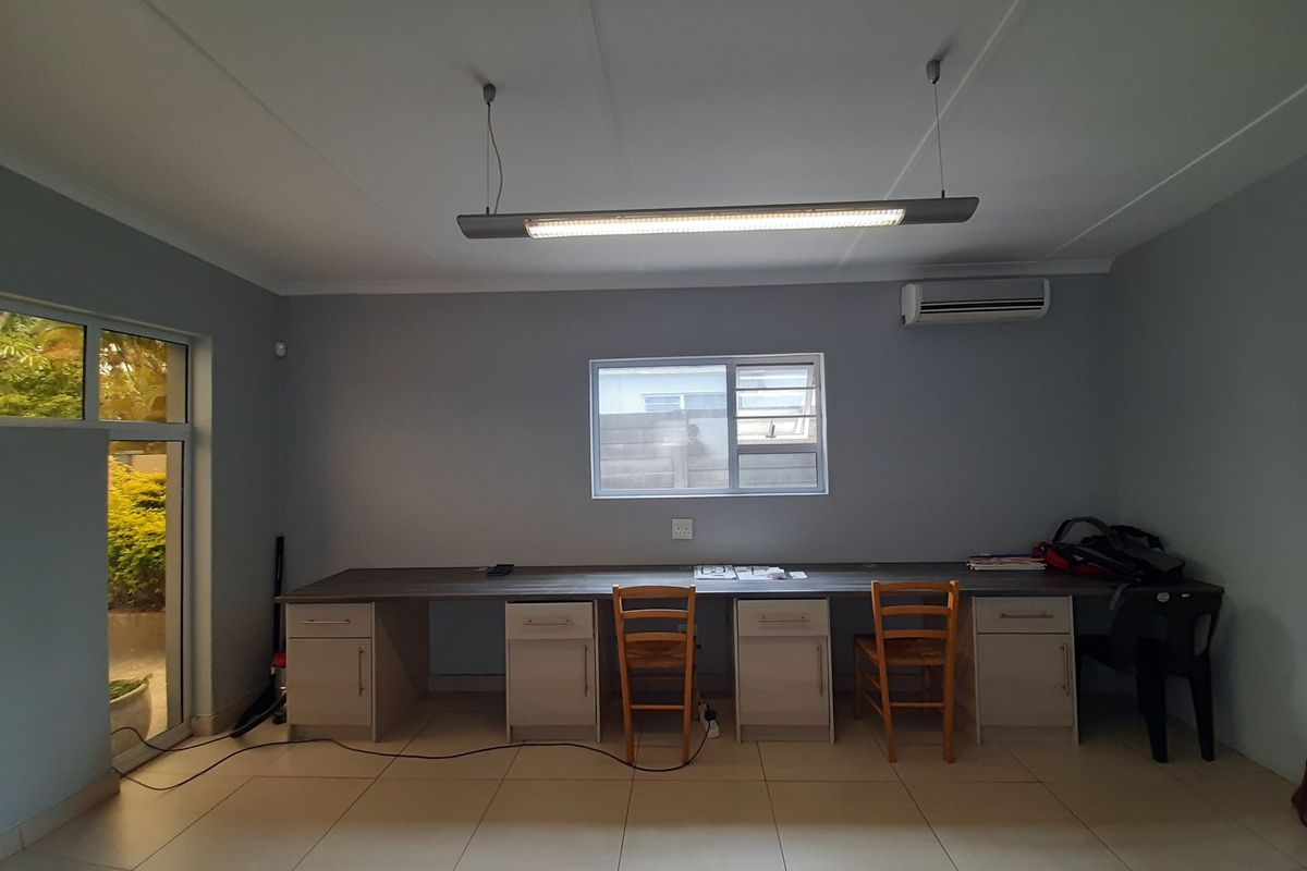 A functional office space featuring a long built-in desk with integrated cabinetry, tiled flooring, air conditioning, and ample natural light from the window and door.