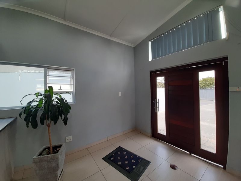 A bright and clean entrance area featuring tiled flooring, a solid timber front door with sidelights, and a high clerestory window for natural light.
