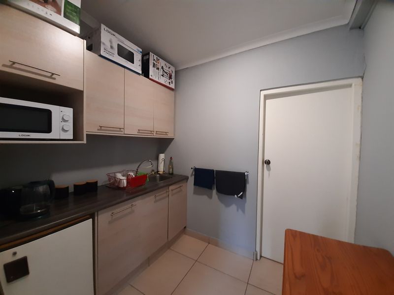 A functional scullery area featuring light wood-tone cabinetry, a stainless steel sink, and tiled flooring, providing practical prep and storage space.