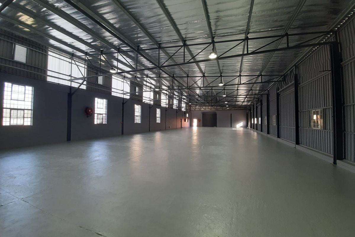 Spacious industrial warehouse featuring high ceilings with exposed steel trusses, polished concrete floors, and ample natural light through multiple windows.