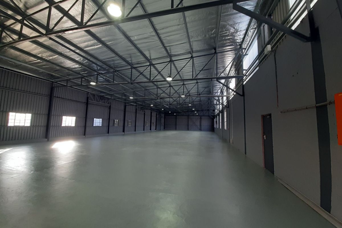 Spacious industrial warehouse unit featuring high ceilings with exposed steel trusses, reflective insulation, durable epoxy flooring, and ample natural light through side windows.