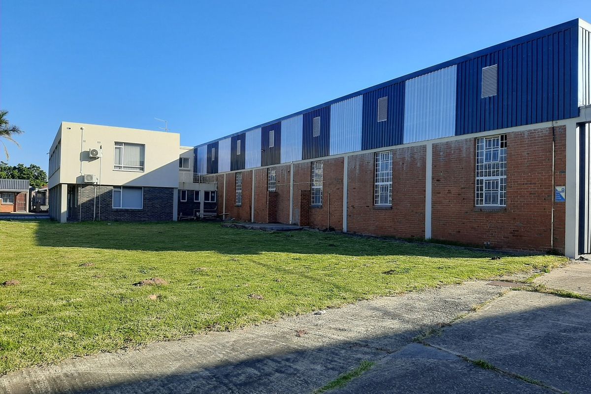 Rear view of an industrial property featuring a brick and metal-clad warehouse structure with an adjacent office section and concrete yard area.
