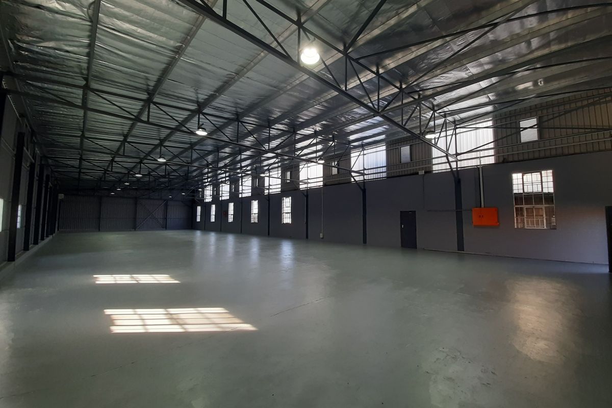 Spacious industrial warehouse unit featuring high ceilings with exposed steel trusses, reflective insulation, polished epoxy flooring, and ample natural light through steel-framed windows.