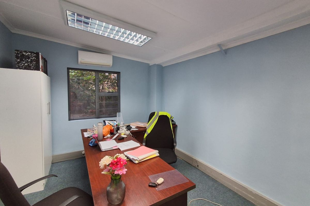A functional office space featuring blue walls, carpeted flooring, recessed ceiling lighting, and a wall-mounted air conditioning unit.
