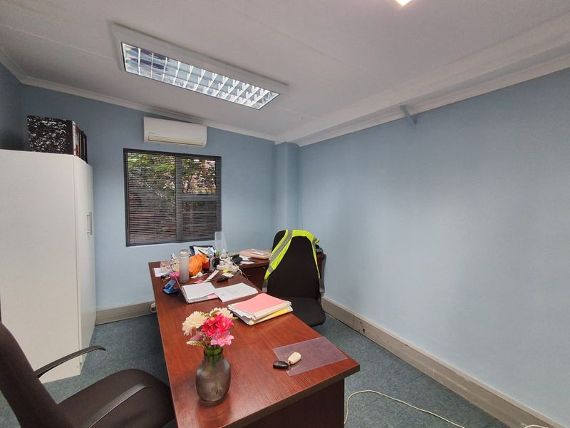 A functional office space featuring blue walls, carpeted flooring, recessed ceiling lighting, and a wall-mounted air conditioning unit.