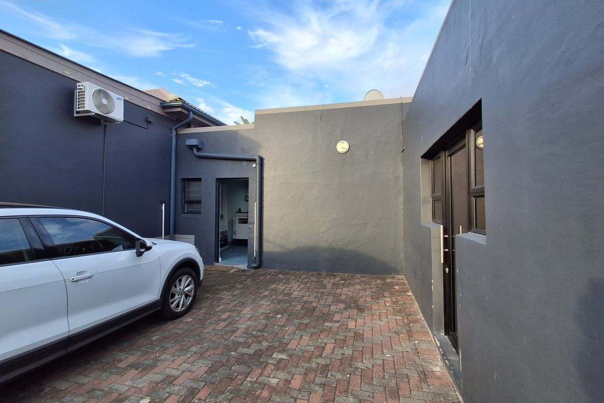 A paved rear courtyard area featuring dark grey exterior walls, integrated air conditioning unit, and access to the office building.