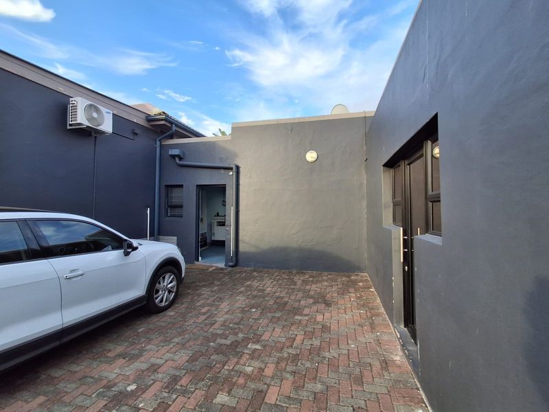 A paved rear courtyard area featuring dark grey exterior walls, integrated air conditioning unit, and access to the office building.