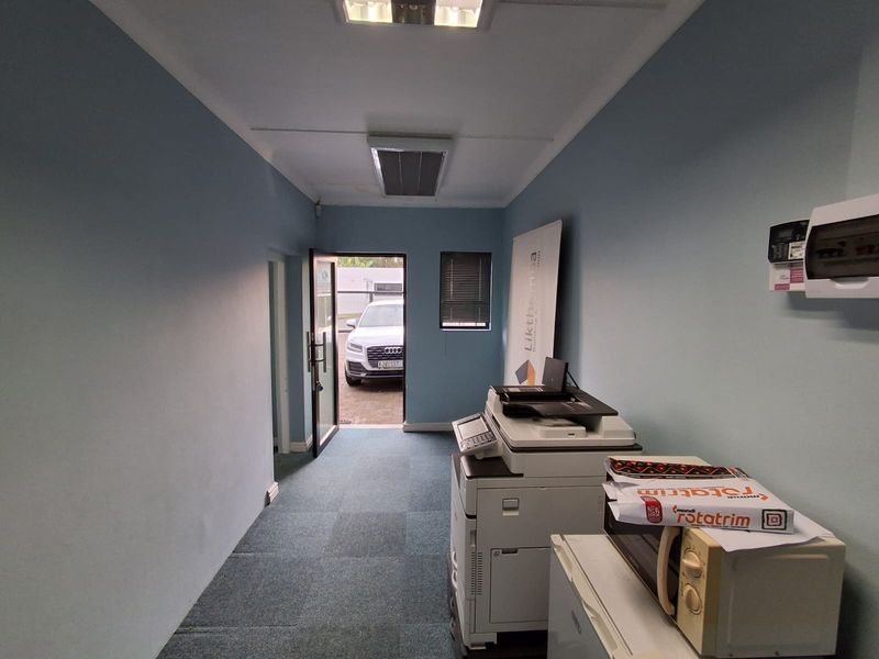 A functional office space featuring carpeted flooring, recessed ceiling lighting, integrated air conditioning, and a wall-mounted electrical distribution board.