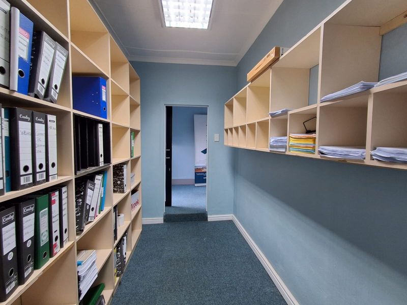 A functional office storage room featuring extensive built-in shelving units, carpeted flooring, and a recessed ceiling light fixture.