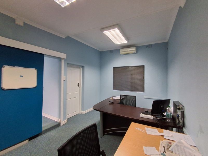 A functional office space featuring blue walls, carpeted flooring, a split-system air conditioner, and integrated lighting, suitable for a professional work environment.