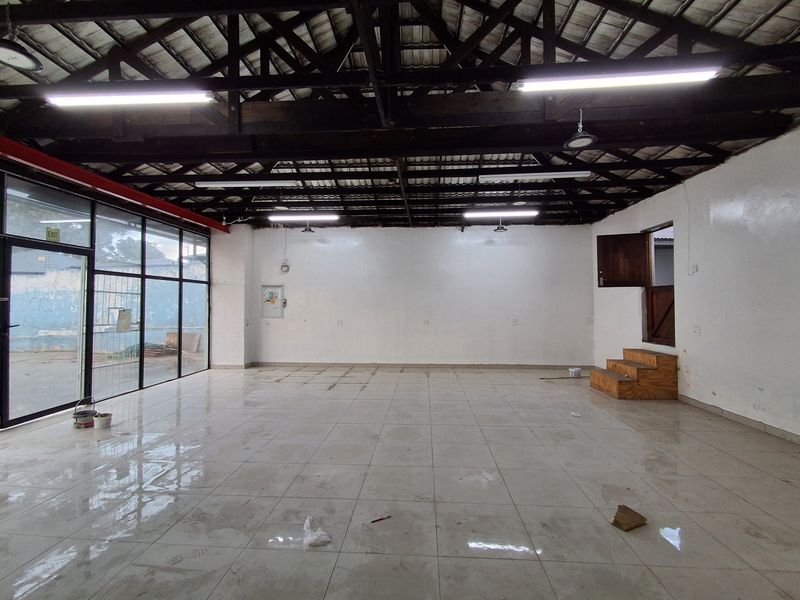 Spacious open-plan retail area featuring high exposed timber ceilings, large glass storefront windows, and durable tiled flooring, suitable for various commercial uses.