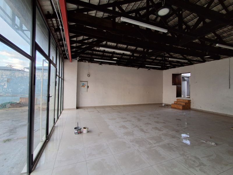 Spacious open-plan retail area featuring high exposed timber roof trusses, large glass storefront windows, and tiled flooring, offering a versatile commercial layout.