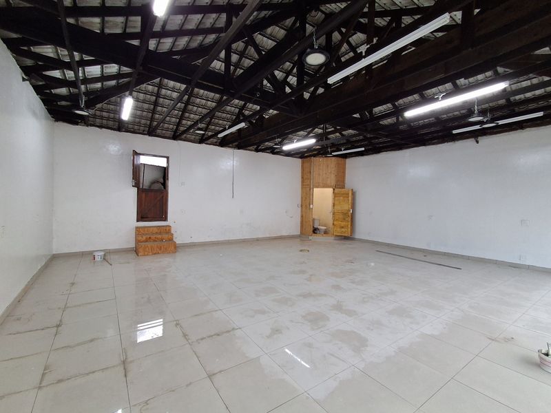 Spacious open-plan retail area featuring exposed timber roof trusses, tiled flooring, and a built-in wooden partition with an integrated restroom.