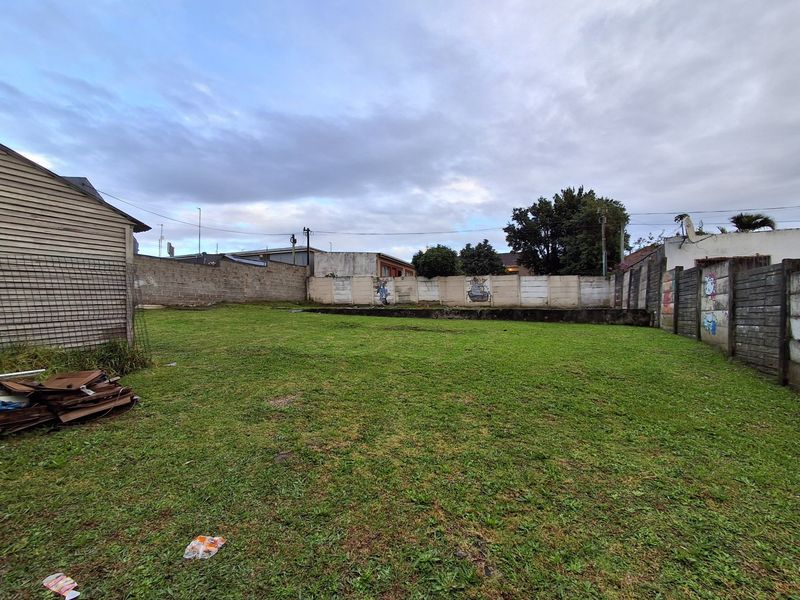 A spacious rear yard area enclosed by precast concrete boundary walls, featuring a grass lawn and visible graffiti on the perimeter fencing.