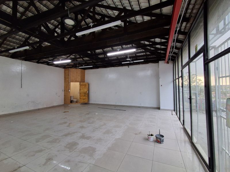 Spacious open-plan retail unit featuring exposed timber roof trusses, large glass storefront windows, tiled flooring, and a private internal toilet cubicle.