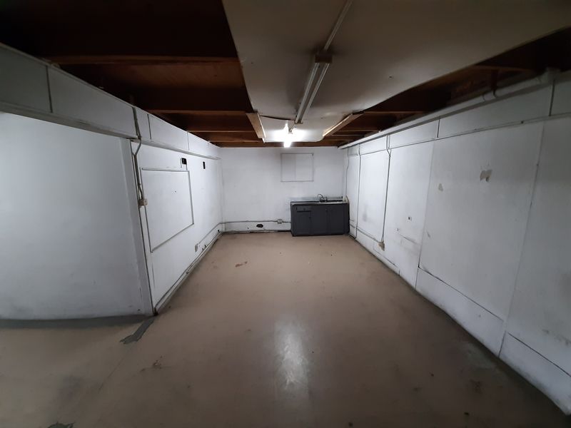 An industrial utility space featuring exposed timber ceiling joists, basic kitchenette cabinetry with a sink, and exposed electrical infrastructure.