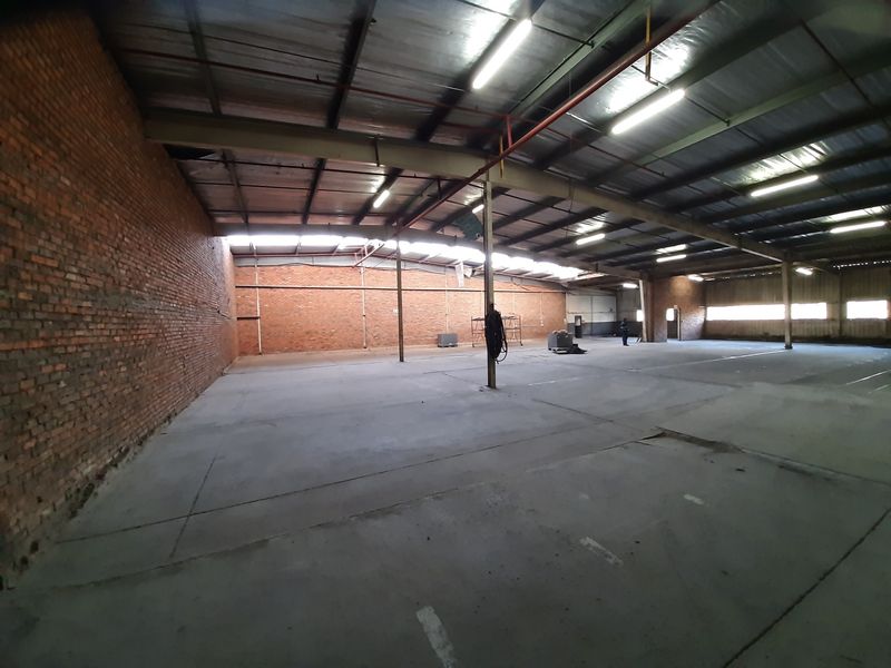 Spacious industrial warehouse unit featuring exposed brick walls, concrete flooring, and high-clearance steel roof trusses with overhead fluorescent lighting.