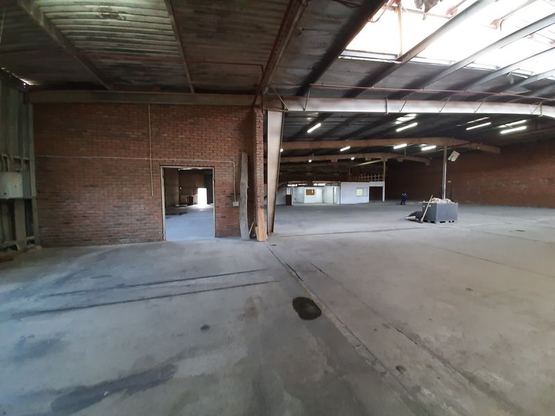 Expansive industrial warehouse space featuring exposed brick walls, high steel truss ceilings with integrated skylights, and durable concrete flooring throughout.