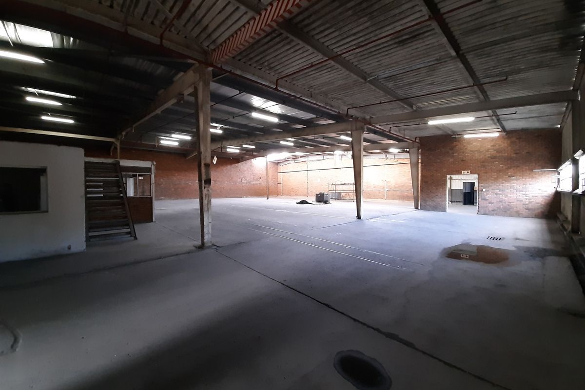 Spacious industrial warehouse featuring exposed brick walls, concrete flooring, and high steel-truss ceilings with integrated lighting and fire sprinkler systems.