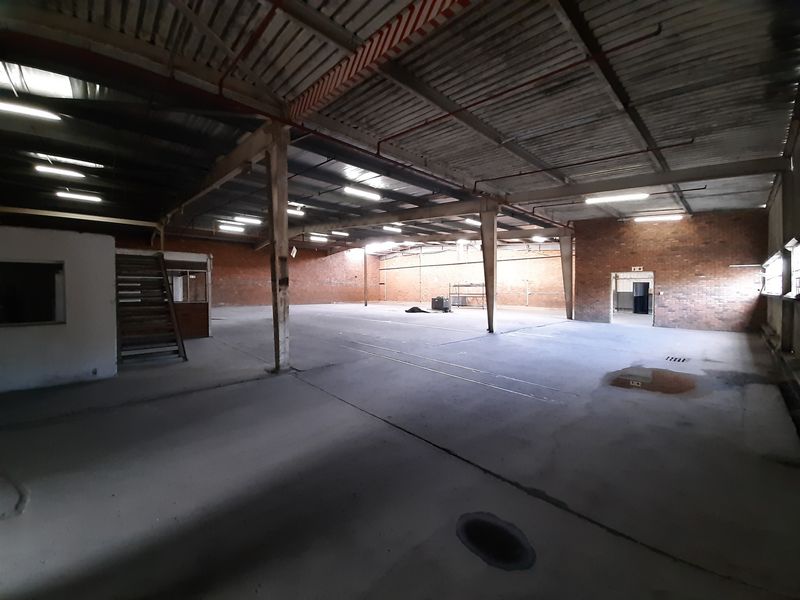 Spacious industrial warehouse featuring exposed brick walls, concrete flooring, and high steel-truss ceilings with integrated lighting and fire sprinkler systems.