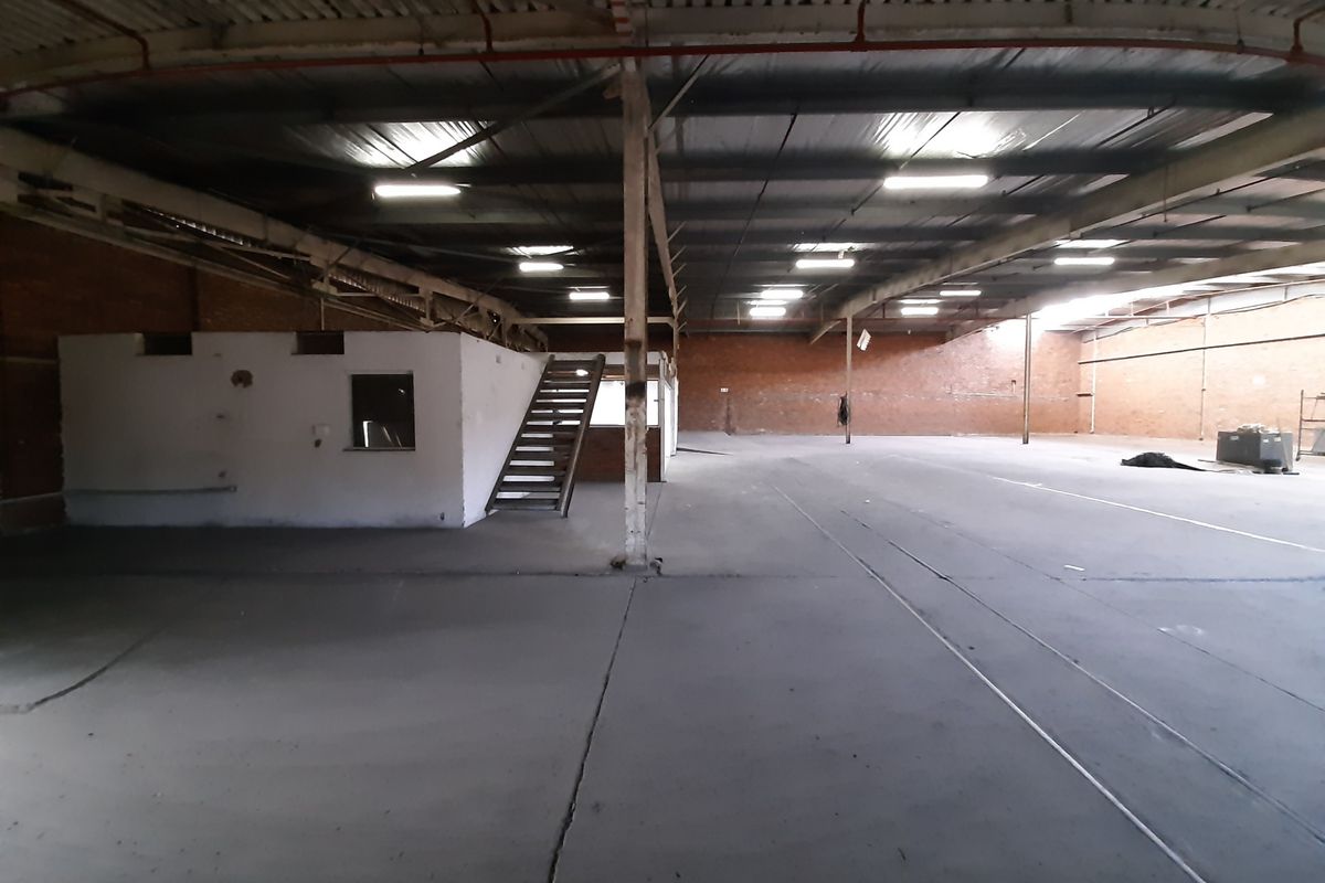 Expansive industrial warehouse space featuring high ceilings with exposed steel trusses, concrete flooring, and a mezzanine level with an integrated metal staircase.